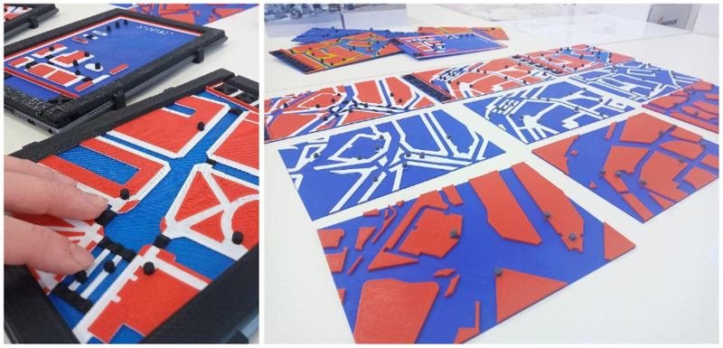 The picture is composed of two kinds of tactile maps. The tactile maps consist of different parts and are marked with the following colours: red, blue, white and black. On the left is a detail of the interactive tactile maps that are attached to the tablet. On the right are the non-interactive tactile maps side by side. They look similar to the interactive ones, but do not have conductive filaments in them and do not attach to the tablet.