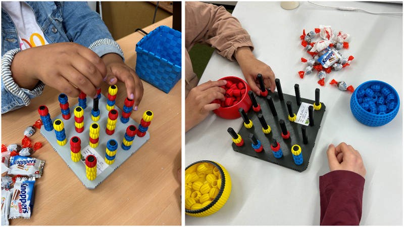 Spiel steht mittig auf einem Tisch, zwei Spielende, von denen man nur die Hände sieht, sitzen drumherum und ertasten die Spielsteine. Neben dem Spiel liegen Süßigkeiten.