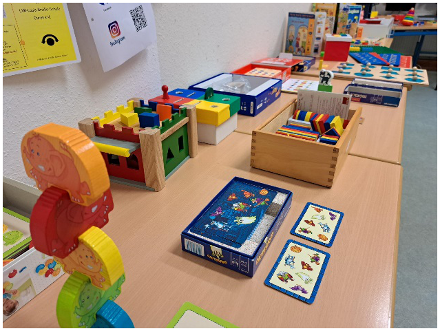 Verschiedene Spielmaterialien aus dem Kitabereich, z.B. logische Blöcke, Stapelelefanten, Gruselino, die auf Tischen präsentiert werden.