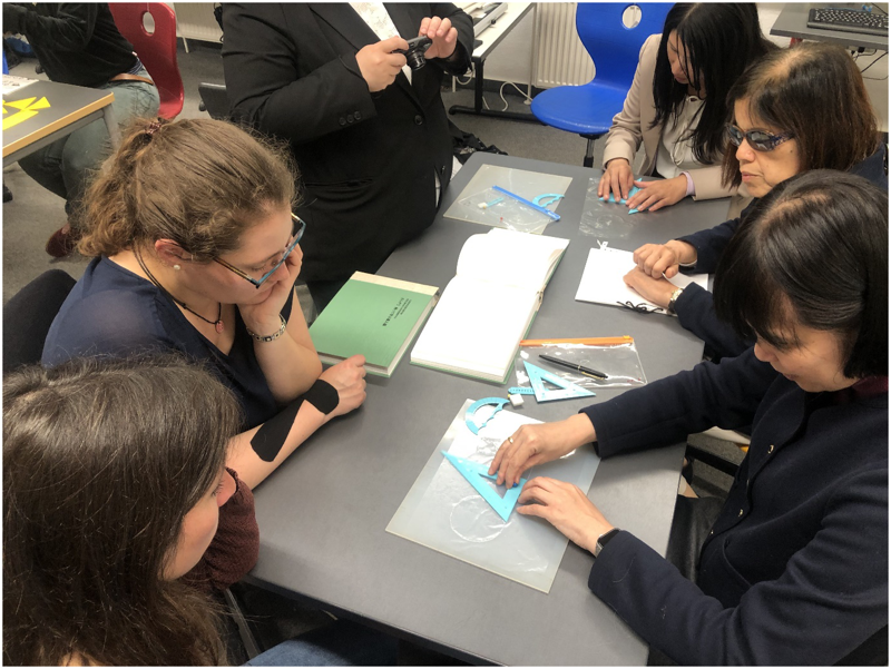 Lehrerinnen aus Japan und des Betty-Hirsch-Schulzentrums der Nikolauspflege tauschen sich in einem Klassenzimmer über Hilfsmittel im Bereich Geometrie aus.