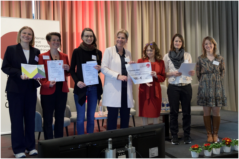Das Foto zeigt sowohl Mitglieder des Forschungsteams aus dem Projekt SuHB als auch die Mitarbeiterinnen der Stiftung Leben pur sowie die Vertreterin des Sponsors für den Preis. Alle Beteiligten sind auf der Bühne; sie präsentieren die Urkunden und die Broschüre mit großer Freude.