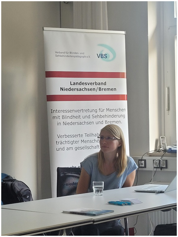 Die Referentin im Rahmen der Landesversammlung, Frau Dr. Susanne Peschke, sitzt vor einem VBS-Aufsteller des Landesverbands Niedersachsen/Bremen. Darauf zu lesen: Landesverband Niedersachsen/Bremen. Interessenvertretung für Menschen mit Blindheit und Sehbehinderung in Niedersachsen und Bremen.