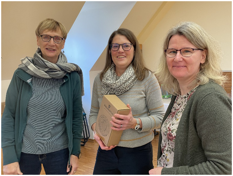 Abb.1 zeigt von links nach rechts Mechthild Gahbler, Barbara Wahl und Imke Wißmann. Alle drei lächeln in die Kamera. Barbara Wahl hält einen Geschenkkarton in ihren Händen. Im Hintergrund sieht man den Raum mit einer Dachschräge.