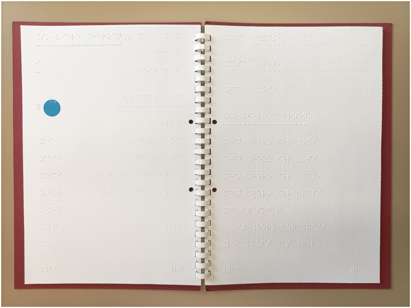 Doppelseite der in Punktschrift übertragenen Auer-Fibel mit einem blauen Klebeetikett für den PennyTalks-Hörstift