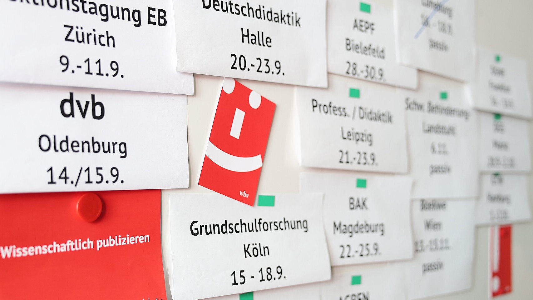 Planung der wbv-Veranstaltungen im September: An einer Wand hängen Karten mit Tagungsorten und Terminen, darunter Zürich, Oldenburg, Köln, Halle, Leipzig und Magdeburg. Dazwischen sind rote wbv-Materialien zu sehen